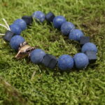 Aetheria Vigor - Einzigartiges Perlenarmband mit Dumerorierit, Onyx, Bergkristall und bronzenem Widderkopf: Dieses kraftvolle Schmuckstück vereint Dumerorierit für Erdung, Onyx für Selbstbeherrschung, Bergkristall für mentale Klarheit und einen bronzenen Widderkopf als Symbol des inneren Kriegergeistes. Spirituelle Verbindung durch die Zeiten: Die Wikingerzeit inspiriert den Widderkopf, während die Steine, in Harmonie kombiniert, Sternzeichen wie Widder, Stier und Steinbock stärken und spirituelle Erkenntnisse fördern. Faszination in Eleganz: Trage "Aetheria Vigor" mit Freude als nicht nur ästhetisches Accessoire, sondern als Begleiter auf deiner spirituellen Reise, der die Kräfte von Erde, Selbstbeherrschung, Klarheit und Kriegergeist vereint.