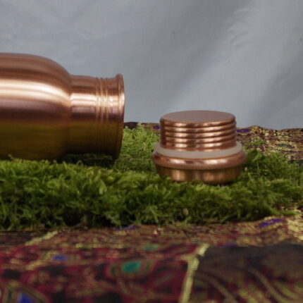 Die 'Copper Serenity Elegance' - eine Kupferflasche, die mehr ist als nur ein Gefäß. Mit ihrer erhabenen Höhe von 27,5 cm und der matten satinierten Politur strahlt sie zeitlose Eleganz aus. Die Oberfläche, empfindlich und doch charmant, erzählt Geschichten von jeder Begegnung mit Wasser und Haut. Dieses Bild erfasst den Moment, in dem Funktion auf Stil trifft – ein visuelles Fest für die Sinne.