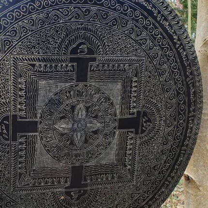 Klangs mit unserem 70 cm großen, voll lackierten Messing-Gong – ein wahres Kunstwerk für die Sinne. Die Vorderseite, gehalten in einer geheimnisvollen grünlichen antiken Farbe auf schwarzem Hintergrund, ist über und über mit kunstvollen, handgeritzten Motiven geschmückt. Ein Quadrat, aus dem ein schimmerndes Kreuz hervorzutreten scheint, dominiert das Zentrum und erzählt Geschichten von zeitloser Harmonie.