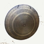 die Schönheit des Klangs mit unserem prachtvollen Bronce-Gong. Ein Kunstwerk aus der Mitte strömender Dreiecke, die sich spiralförmig nach außen verteilen und in kunstvoll verzierten Ringen enden, auf denen ein heiliges Mantra in Sanskrit ruht. Über allem thronen faszinierende Verzierungen, die diesem majestätischen Instrument eine Aura der Erhabenheit verleihen.